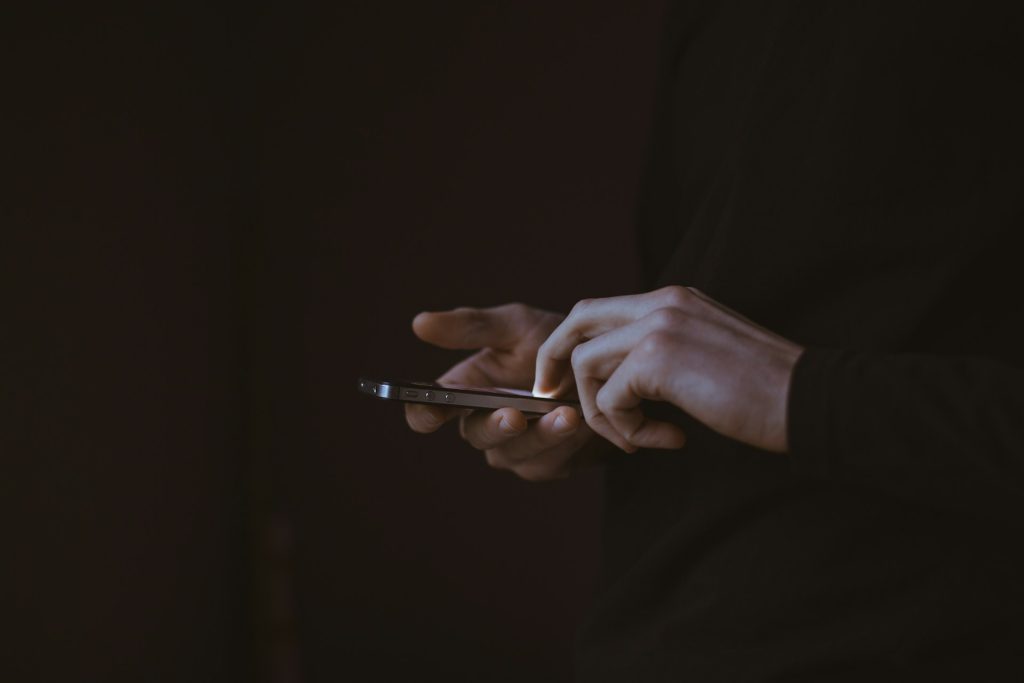 hands holding phone on dark background symbolizing synthetic fraud